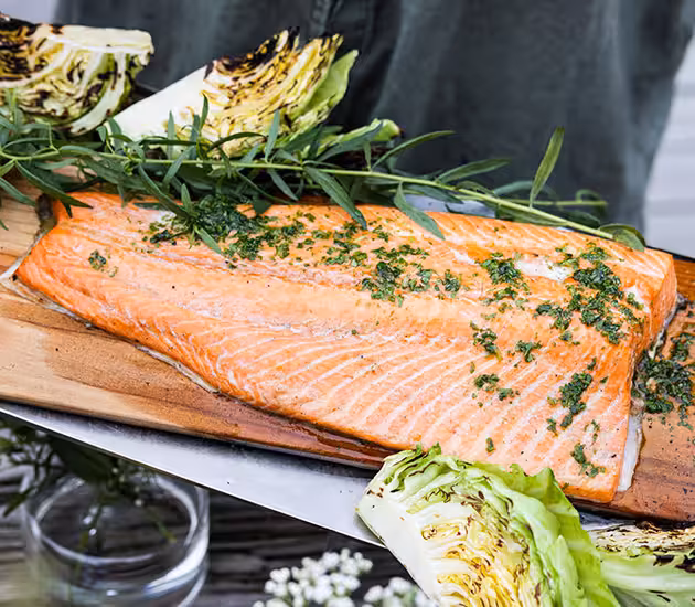 Grilled salmon on a plank with herb oil, potatoes and grilled cabbage