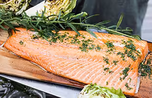 Grilled salmon on a plank with herb oil, potatoes and grilled cabbage